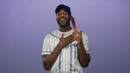 Man wearing pinstripe jersey and blue cap holding baseball bat over shoulder and pointing finger to chest in purple studio; gratitude.