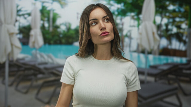 Woman holds open palm by hotel building at a resort pool beside white lounge chairs and folded umbrellas; serenity. - Powered by Adobe