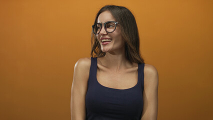 Woman smiling with glasses and bare shoulders turning head with long brown hair in orange studio; confidence.