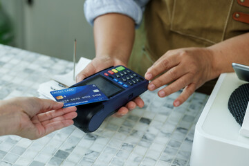 Credit card hovering above payment terminal on coffee shop counter, barista assisting customer to complete cashless payment process in cozy family-run independent cafe, Concept small business