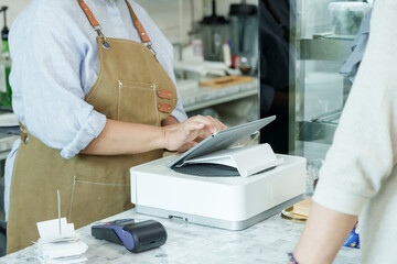 Asian senior female barista adult assisting customer using point-of-sale system at cafe counter representing friendly professional service in local small family coffee shop environment