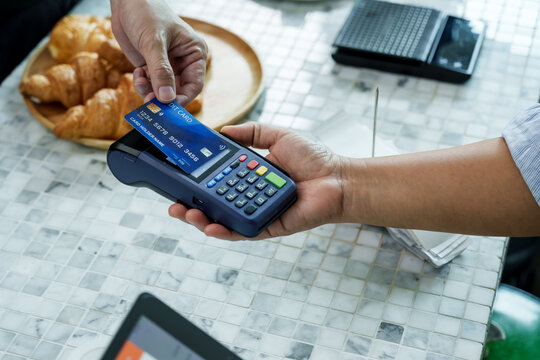 Customer’s card and terminal at coffee shop counter during cashless transaction, barista assisting to ensure smooth payment experience in small family-run cafe, Concept small business