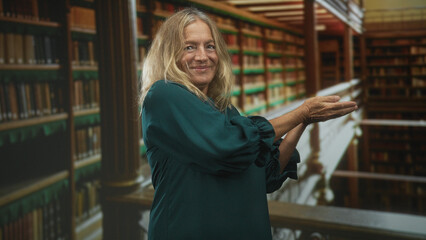 Woman with cupped hands presenting bookshelves in an ornate library building, smiling and gesturing palm up; knowledge sharing serenity.