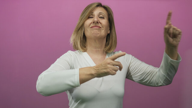 Middle age caucasian woman smiling with raised index finger pointing upward in pink studio; confidence.