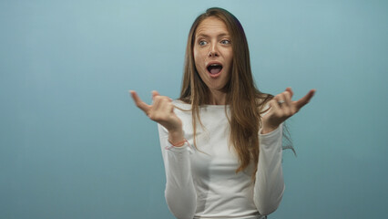 Fototapeta premium Woman with hands and fingers beckoning toward camera in blue studio wearing a white top, young adult with animated facial expression; surprised.