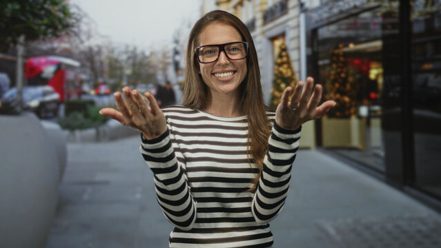 Woman with open palms reaching out on street amid city storefronts and blurred traffic; happy welcome.