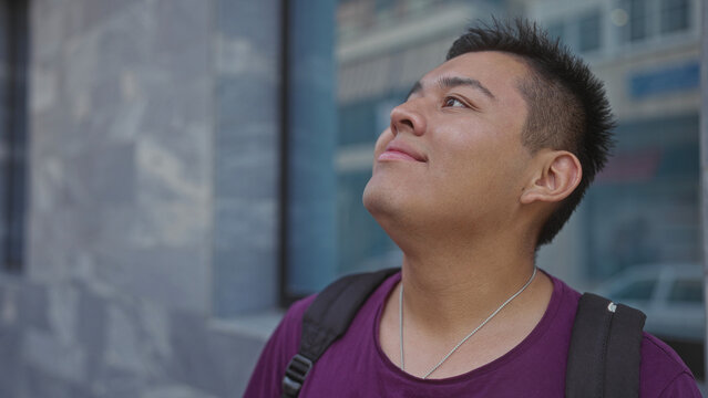 Man tilts head upward, eyes open, backpack on shoulder beside building window on street; serenity reflection. - Powered by Adobe
