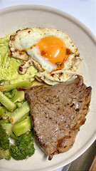 Grilled steak with fried egg, mashed avocado and broccoli on plate, savory homemade breakfast