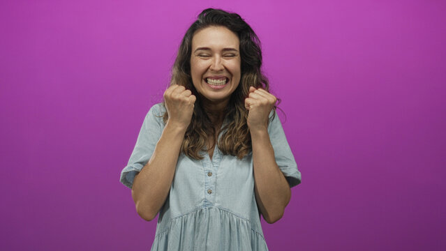 Hispanic woman raises clenched fists and spreads open palms in a vibrant purple studio scene; excitement triumph celebration.