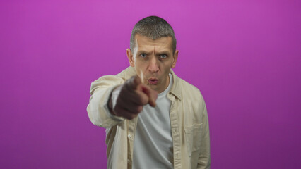 Caucasian man gesturing energetically toward camera against vibrant pink background wearing casual beige shirt conveying emotion and expression.