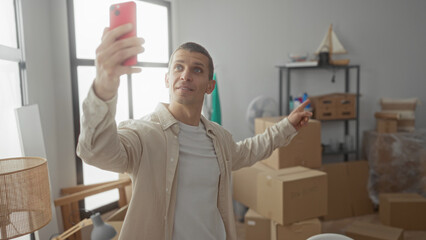 Man smiling during videocall in bright living room surrounded by cardboard boxes showing recent move into new apartment.