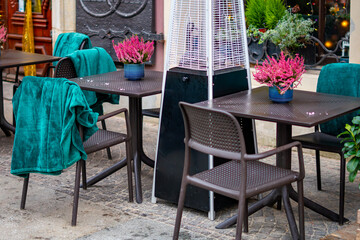 Café outdoor tables with brown chairs, teal blankets and heather pots arranged around a standing patio heater unit