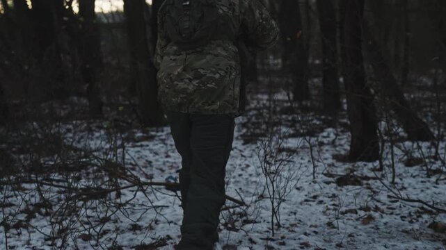 Soldier on a military recon mission in the wilderness. Forest full of snow at winter. Soldier reloading then walking through the snow