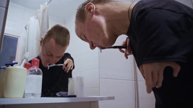 Man with achondroplasia doing his morning routine, brushing his teeth in front of a mirror
