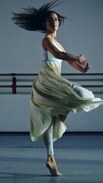Slow motion vertical shot of graceful contemporary female dancer practices with focus and elegance in dance school or gym, refining her technique and expression through rigorous training, dedication.