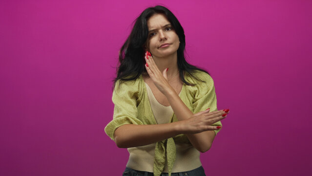 Young hispanic woman standing with firm posture makes arms crossed x gesture in pink studio; rejection defiance.