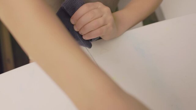 Close up of a child learning to sew by hand, practicing stitching and holding fabric with both hands. Early skill building, concentration, and fine motor development. Concept of patience, home