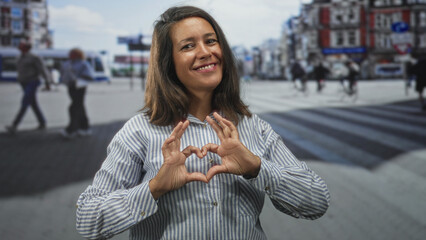 Woman making heart with hands at street crosswalk, striped shirt and smiling brunette in urban...