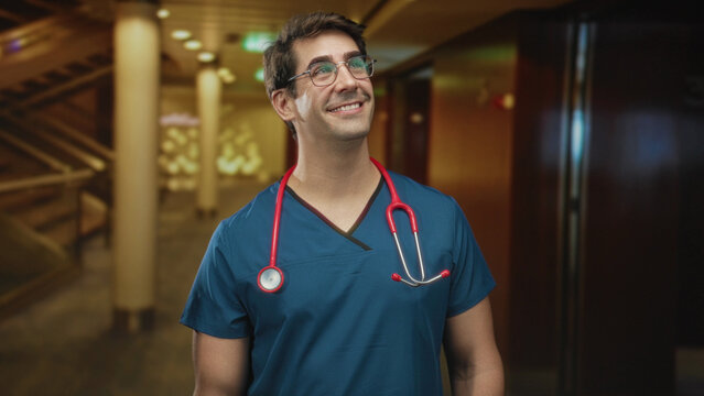 Man doctor in blue scrubs smiles holding a red stethoscope in a building; compassion recovery trust.