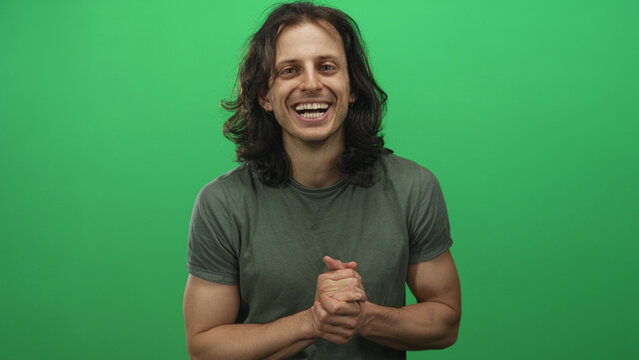 Young hispanic man with long hair clapping hands and smiling in studio before green screen; joy celebration. - Powered by Adobe