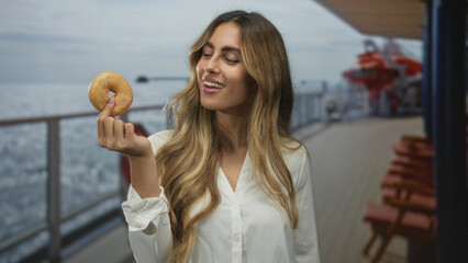 Woman holding donut with hand on cruise ship deck near railing smiling with closed eyes; pleasure...
