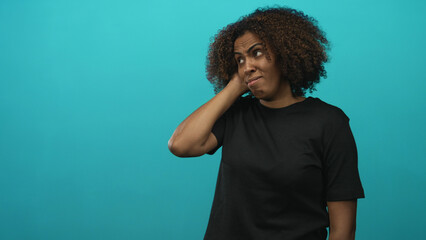 Woman with hand on neck and raised eyebrow in studio against a teal wall showing a puzzled...
