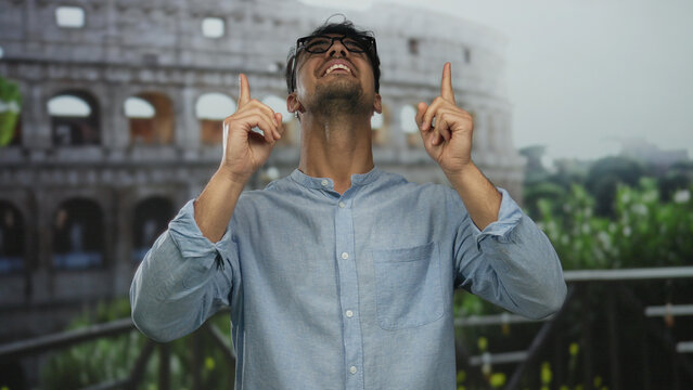 Young man in blue shirt pointing upwards with excitement near roman coliseum, highlighting a vibrant outdoor scene with historic architecture and urban ambiance in rome.