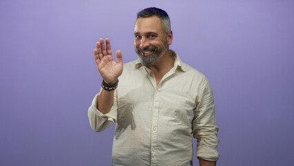 Middle aged hispanic man with salt and pepper beard smiling in purple studio wearing beige linen...