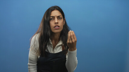 Woman with pinched fingers gesture and tense face in blue studio leaning forward wearing dark...