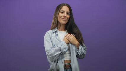 Young woman clasping hands over chest smiling, wearing light blue shirt white crop top and jeans...