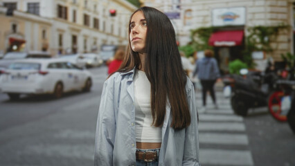 Fototapeta premium Woman with bare midriff and long hair, standing with eyes closed and head tilted up on a street; serenity introspection.