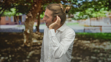 Man in white shirt with raised hand, long hair and thoughtful gaze in green park under sunlight; curiosity.