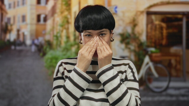 Chinese woman showing discomfort in an urban street setting with blurred background, wearing striped sweater and earrings, facial expression reflects unease and hesitation. - Powered by Adobe
