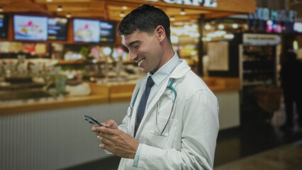 Man doctor wearing lab coat with stethoscope smiling while tapping smartphone in restaurant; happiness.