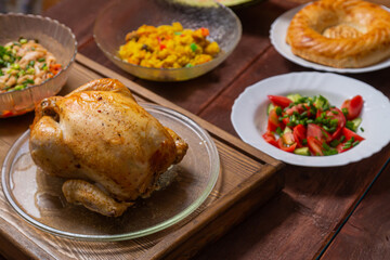 Couscous with dried fruits and turmeric, baked whole chicken, flatbread, and vegetable salad on a wooden table. Horizontal photo.