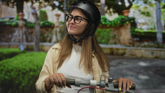 Woman in helmet and glasses holding scooter handlebars while smiling and looking sideways on street; confidence urban commute.