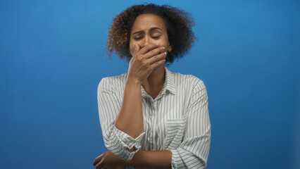 Woman in striped shirt with hand covering mouth in blue studio, hunched forward with pained expression; nausea distress.