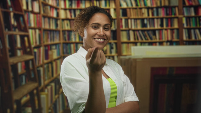 Woman beckons finger toward viewer inside library building, smiling with crossed arms and neon top visible; mischief.