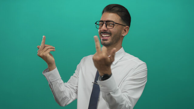 Hispanic man wearing white shirt and blue tie shows two middlefinger gestures in studio with teal backdrop; defiance.