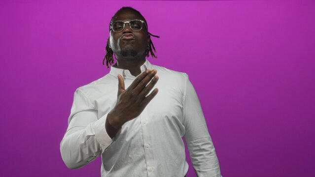 Man pointing thumbs to chest in purple studio wearing white shirt and glasses, facing camera with smirk; confidence assertiveness bold energy.