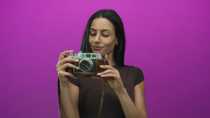 Woman posing with vintage camera in front of vibrant pink background showcasing a playful expression with long hair and casual outfit.