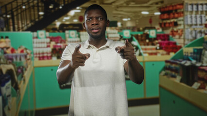 Man points finger at camera with visible fingers and white polo in retail building; assertive challenge.