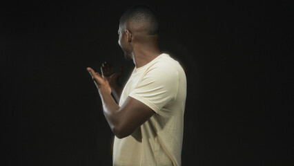 Man gesturing with open hands and visible forearms, smiling in a white t shirt inside a studio set,...