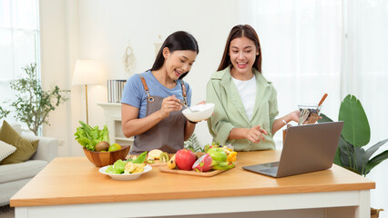 Friends Preparing a Healthy Meal Together in a Bright Kitchen While Using a Laptop for Recipes