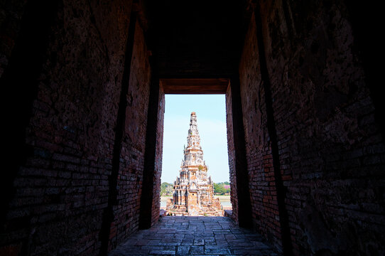 A view of an ancient temple spire framed by a dark brick corridor, with bright sunlight illuminating the temple in the background. - Powered by Adobe