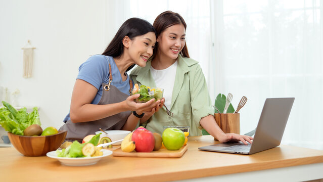 Friends Preparing a Healthy Meal Together in a Bright Kitchen While Using a Laptop for Recipes - Powered by Adobe