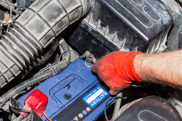 Gloved hands use a wrench to tighten or loosen car battery terminals during vehicle maintenance and...