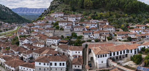Panoramic view of Berat&rsquo;s hillside homes with white fa&ccedil;ades and tiled roofs rising above the river valley and mountain backdrop.
