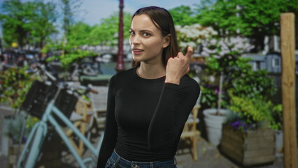 Woman cups her ear and tucks hair by a bicycle and planters on an amsterdam street, gazing sideways...