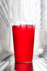 Bright red juice fills a tall glass on a reflective surface, set against a cool, geometric background. Fresh, bold, and appealing, this image suits food, beverage, health, and lifestyle visuals.